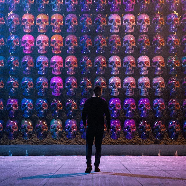 3D render titled 'Día de Muertos', depicting a man observing a vibrant altar of neon-lit skulls, reminiscent of Oaxaca's traditional celebration of life and death