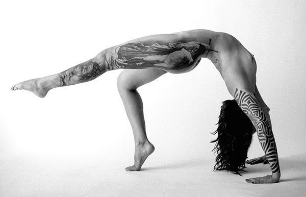 Black and white artistic photography of a tattooed woman arching her body, white background, by Juan Pablo Galguera