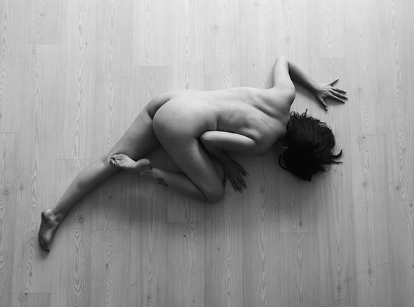 Black and white artistic photography, top-down view of a nude figure on the floor, exotic lizard-like pose, wooden background, by Juan Pablo Galguera