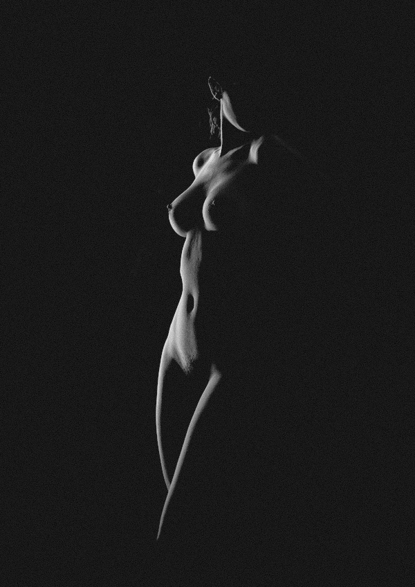 Black and white artistic photo of a nude woman in darkness, front view, lit to show only silhouette, by Juan Pablo Galguera
