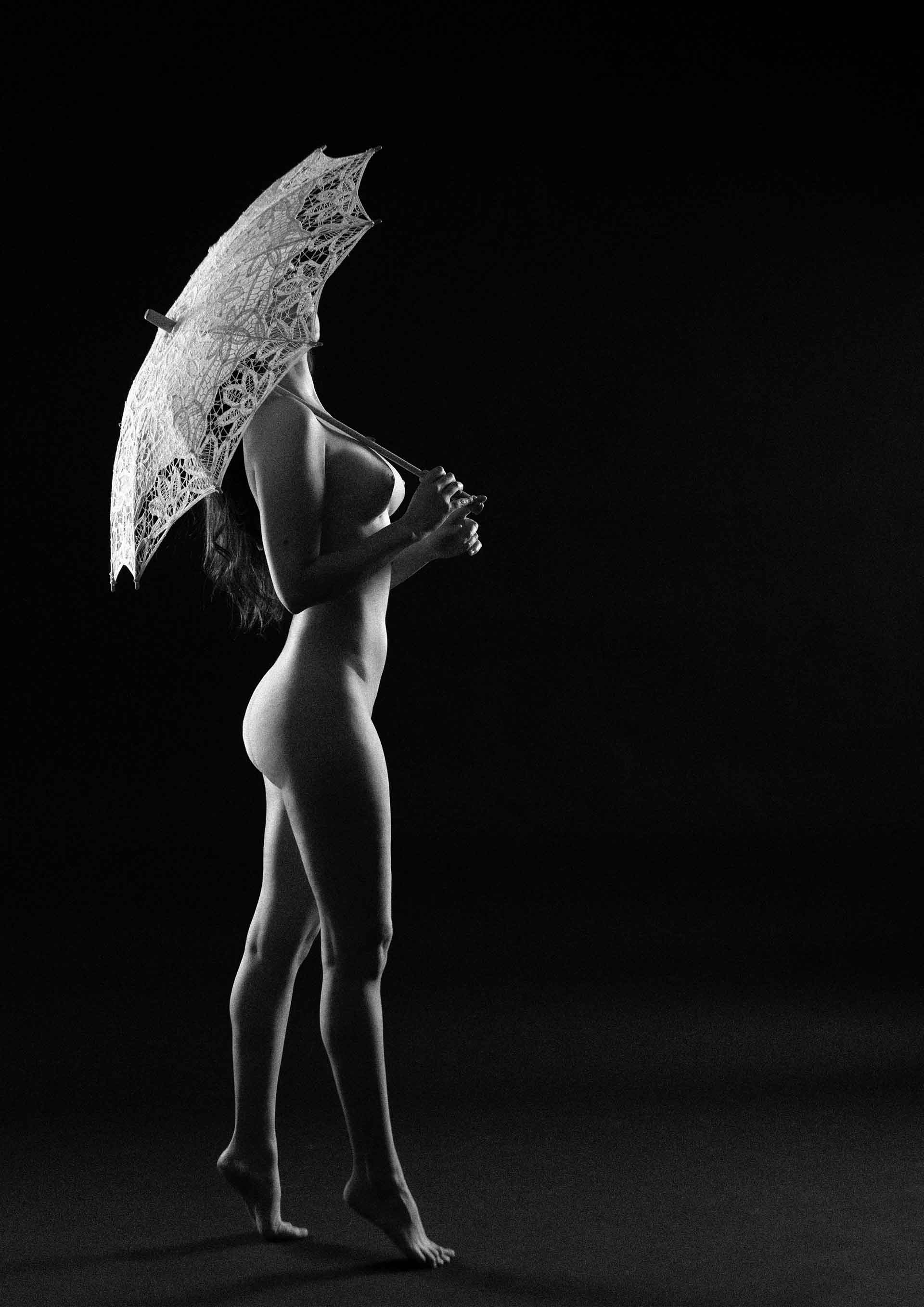 Black and white artistic photography of a nude figure under an lace parasol, by Juan Pablo Galguera